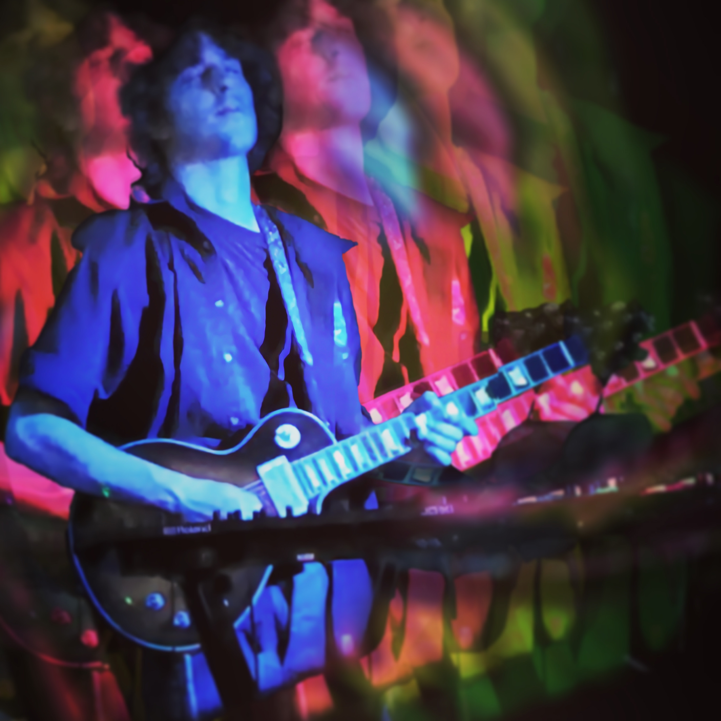 Jay Cotter performing with guitar and keyboard in a colorful layered performance photograph