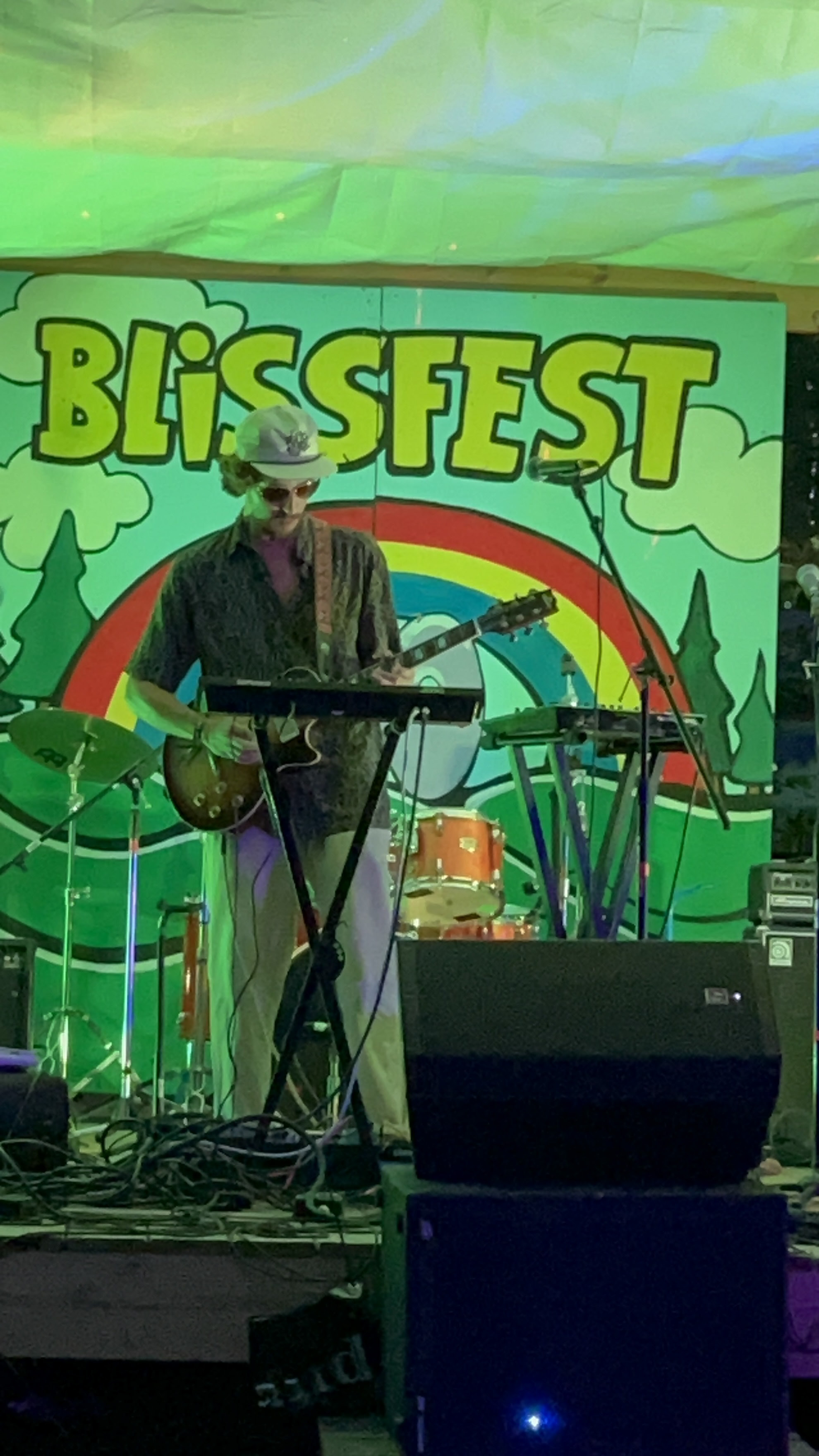 Jay Cotter playing guitar and keyboard on a stage with a Blissfest banner